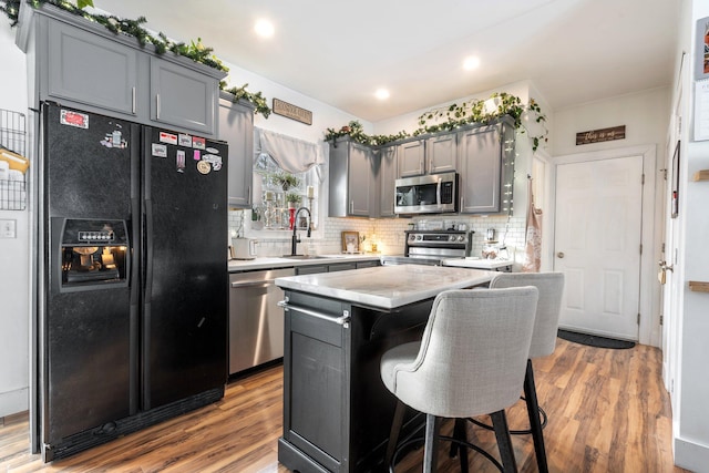 kitchen with gray cabinets, appliances with stainless steel finishes, a kitchen island, a sink, and wood finished floors