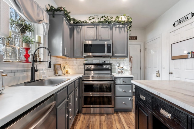 kitchen with stainless steel appliances, a sink, light wood-style floors, light countertops, and decorative backsplash