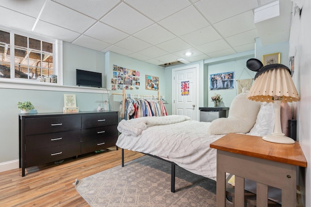 bedroom featuring a closet, light wood-type flooring, a paneled ceiling, and baseboards