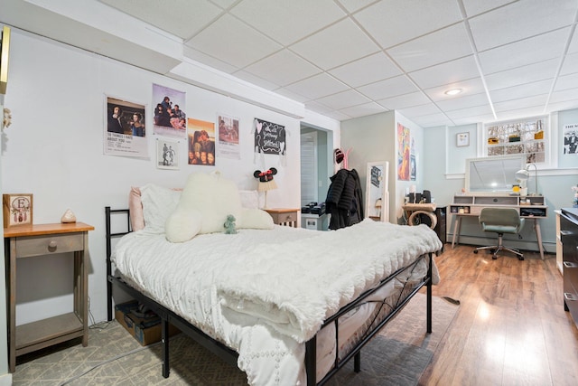 bedroom featuring a baseboard heating unit, a drop ceiling, and wood finished floors