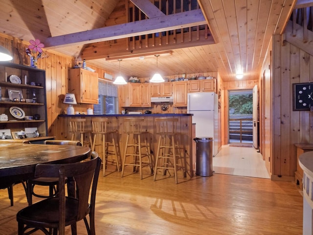 kitchen with freestanding refrigerator, light brown cabinets, wood walls, wooden ceiling, and under cabinet range hood