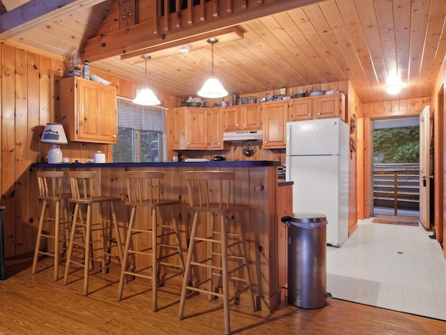 kitchen featuring dark countertops, wooden ceiling, freestanding refrigerator, and under cabinet range hood