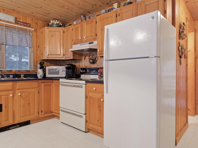 kitchen with under cabinet range hood, white appliances, a sink, light floors, and dark countertops