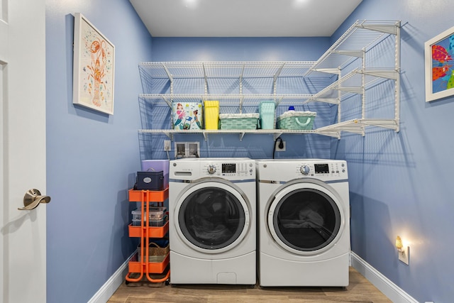 clothes washing area featuring laundry area, separate washer and dryer, wood finished floors, and baseboards