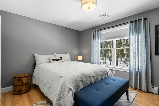 bedroom featuring a baseboard heating unit, light wood finished floors, visible vents, and baseboards