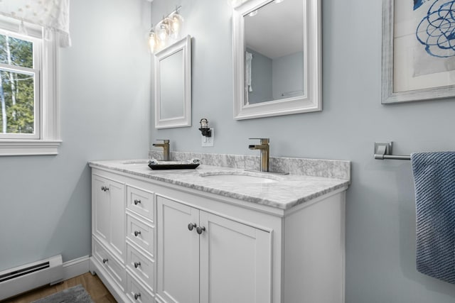 bathroom with double vanity, wood finished floors, a baseboard radiator, and a sink