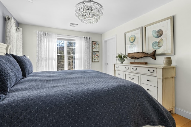 bedroom featuring baseboards, light wood-type flooring, visible vents, and a notable chandelier