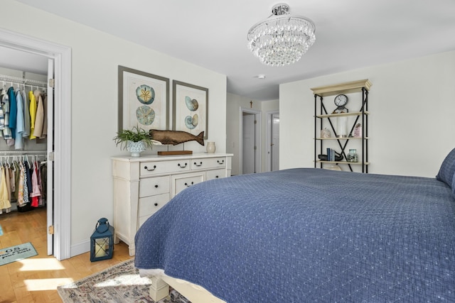 bedroom featuring a closet, a spacious closet, a chandelier, light wood-type flooring, and baseboards