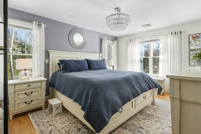 bedroom featuring visible vents, light wood-style flooring, and an inviting chandelier