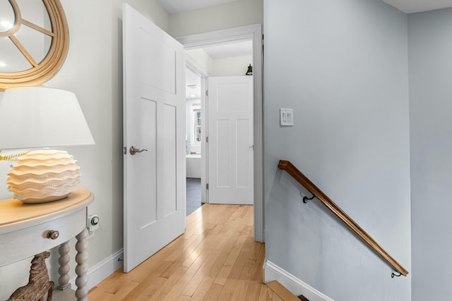 hallway featuring light wood finished floors, an upstairs landing, and baseboards