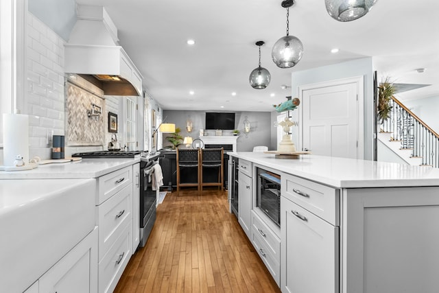 kitchen with black microwave, open floor plan, light countertops, stainless steel gas range, and pendant lighting