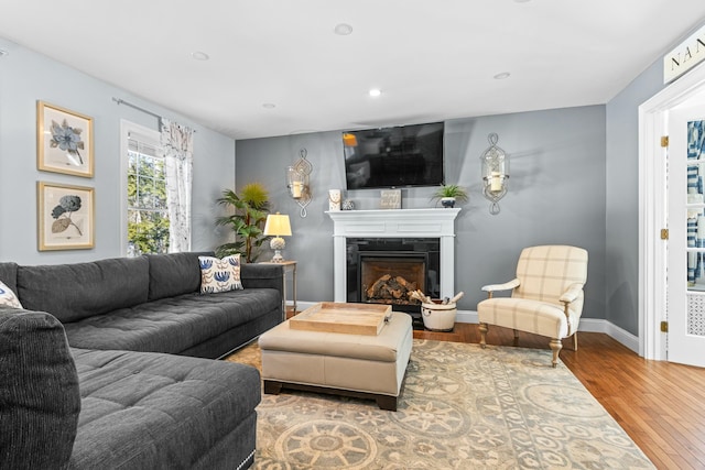 living area featuring a glass covered fireplace, recessed lighting, baseboards, and wood finished floors