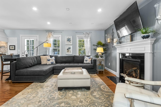 living room featuring a fireplace with flush hearth, recessed lighting, baseboards, and wood finished floors