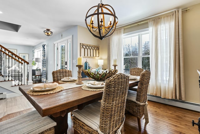 dining room featuring a baseboard heating unit, wood-type flooring, a notable chandelier, and stairs