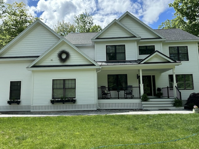 view of front of home featuring covered porch, a shingled roof, a standing seam roof, and a front yard