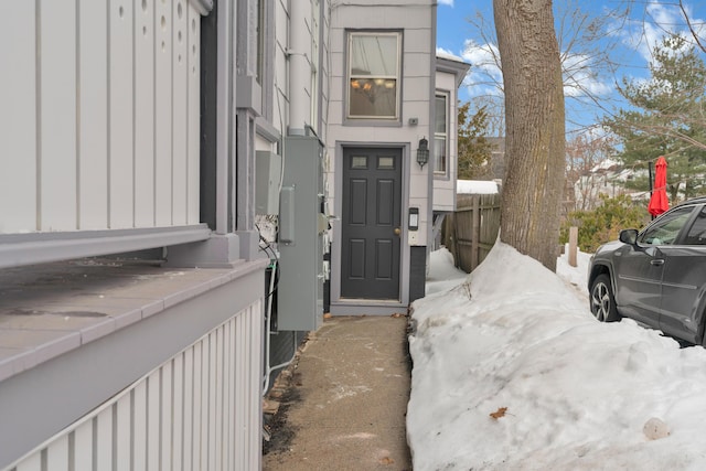 snow covered property entrance with board and batten siding and fence