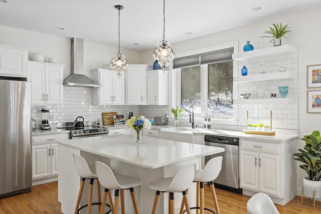 kitchen featuring white cabinetry, appliances with stainless steel finishes, wall chimney exhaust hood, and a breakfast bar