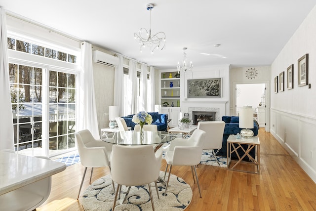 dining space featuring a chandelier, light wood finished floors, a wall mounted AC, and a high end fireplace