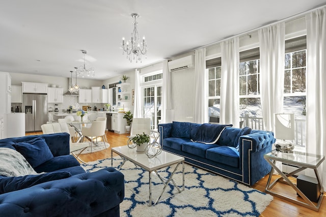 living area with a wealth of natural light, a notable chandelier, light wood-style floors, and a wall mounted AC