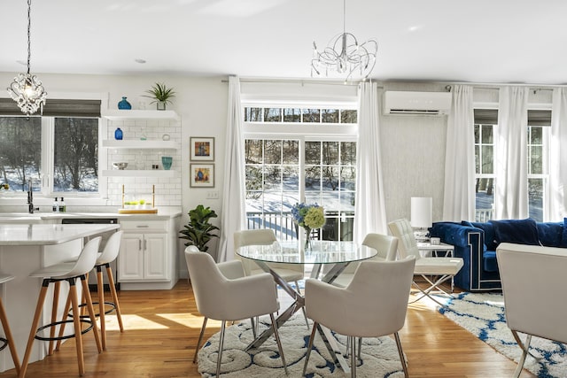 dining room with a wall unit AC, light wood-style flooring, and a chandelier