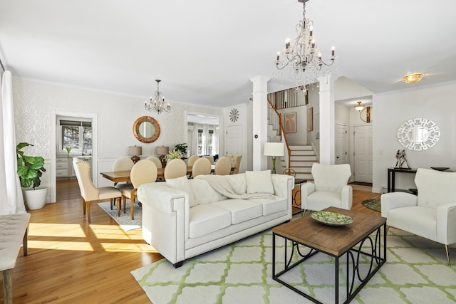 living room with an inviting chandelier, decorative columns, light wood finished floors, and ornamental molding