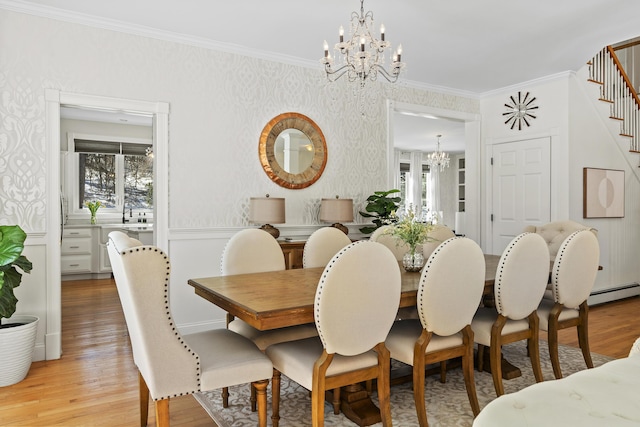 dining area featuring wallpapered walls, a baseboard heating unit, crown molding, light wood-style floors, and a notable chandelier