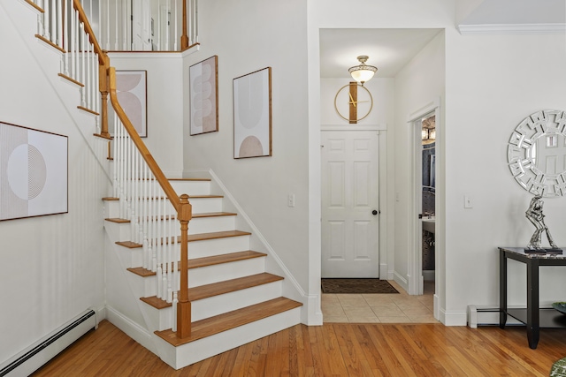 foyer entrance featuring baseboards, light wood-type flooring, a baseboard heating unit, and stairs