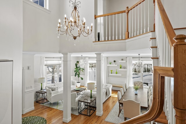 dining area featuring a chandelier, stairway, a high ceiling, wood finished floors, and ornate columns