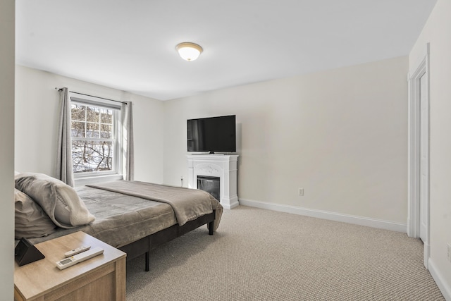 bedroom with baseboards, light colored carpet, and a glass covered fireplace