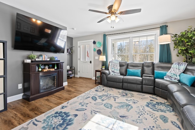 living area with a fireplace, wood finished floors, a ceiling fan, and baseboards