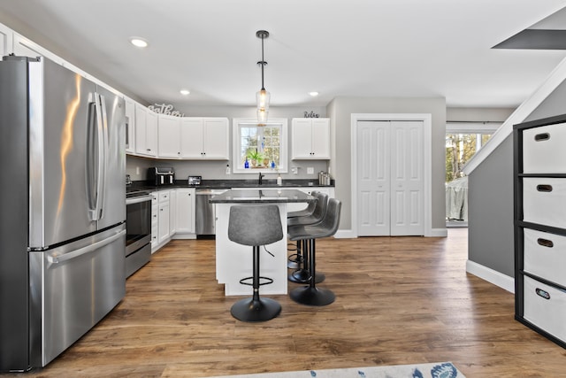 kitchen with dark wood finished floors, dark countertops, a kitchen breakfast bar, stainless steel appliances, and white cabinetry