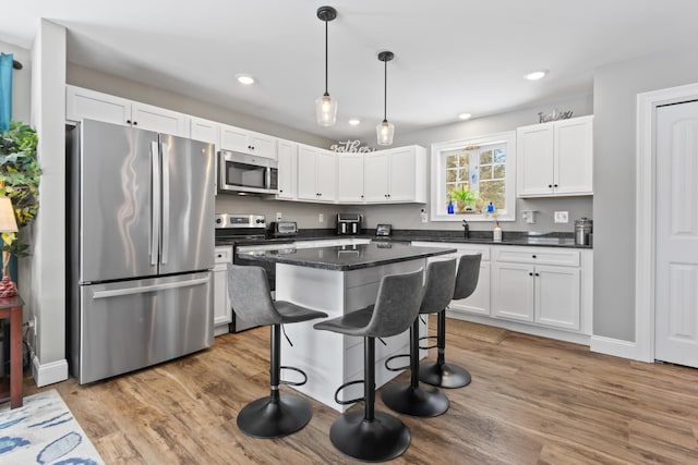 kitchen with light wood finished floors, appliances with stainless steel finishes, a kitchen breakfast bar, a center island, and white cabinetry