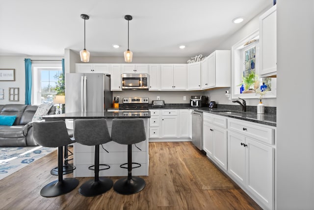 kitchen with a breakfast bar area, wood finished floors, stainless steel appliances, white cabinetry, and a sink