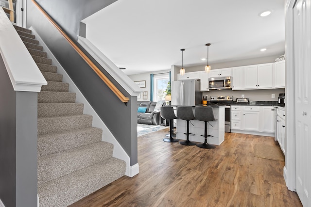 kitchen featuring wood finished floors, white cabinetry, a kitchen breakfast bar, appliances with stainless steel finishes, and dark countertops