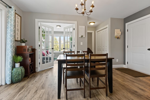 dining area featuring baseboards, french doors, wood finished floors, and a notable chandelier