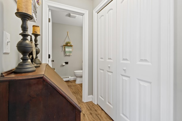 corridor with light wood-type flooring, a baseboard radiator, and baseboards