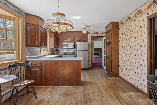 kitchen with appliances with stainless steel finishes, a sink, light wood finished floors, a peninsula, and a healthy amount of sunlight