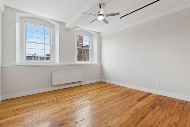 empty room featuring baseboards, light wood finished floors, beamed ceiling, and radiator