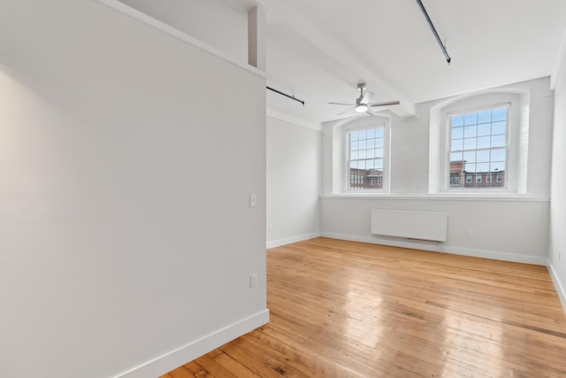 empty room featuring a ceiling fan, baseboards, light wood-style flooring, and radiator heating unit