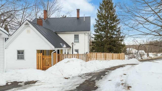 snow covered back of property featuring a chimney, fence, and metal roof