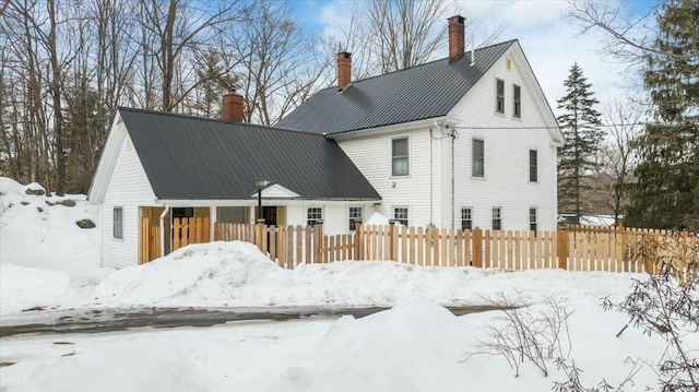 snow covered house with a fenced front yard, metal roof, and a chimney