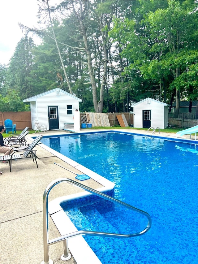 view of pool featuring a fenced in pool, fence, a storage structure, a patio area, and an outbuilding