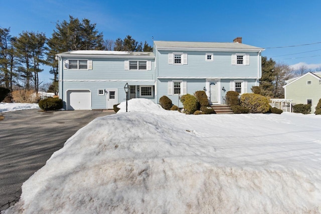 colonial house featuring aphalt driveway, an attached garage, and a chimney