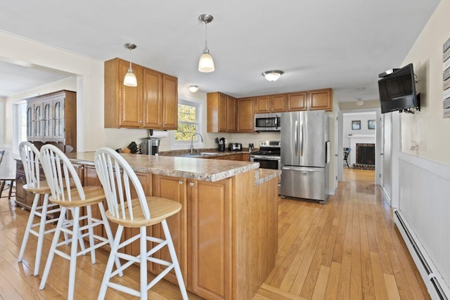 kitchen with light wood-style floors, baseboard heating, appliances with stainless steel finishes, and a peninsula