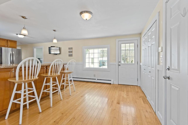 dining room featuring light wood finished floors, baseboard heating, and wainscoting