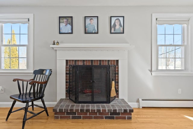 interior details featuring a fireplace, a baseboard heating unit, baseboards, and wood finished floors