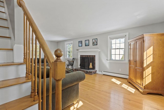 living room with a baseboard radiator, light wood-style flooring, a fireplace, and stairway