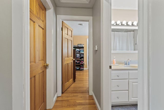 hallway featuring a sink, baseboards, and light wood finished floors