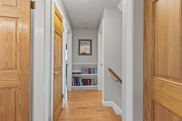 corridor with an upstairs landing, baseboards, and light wood finished floors