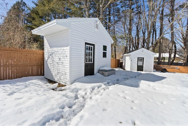 snow covered structure featuring an outbuilding and fence